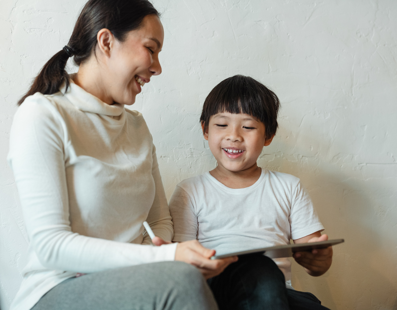 Crop ethnic mother browsing tablet with glad child